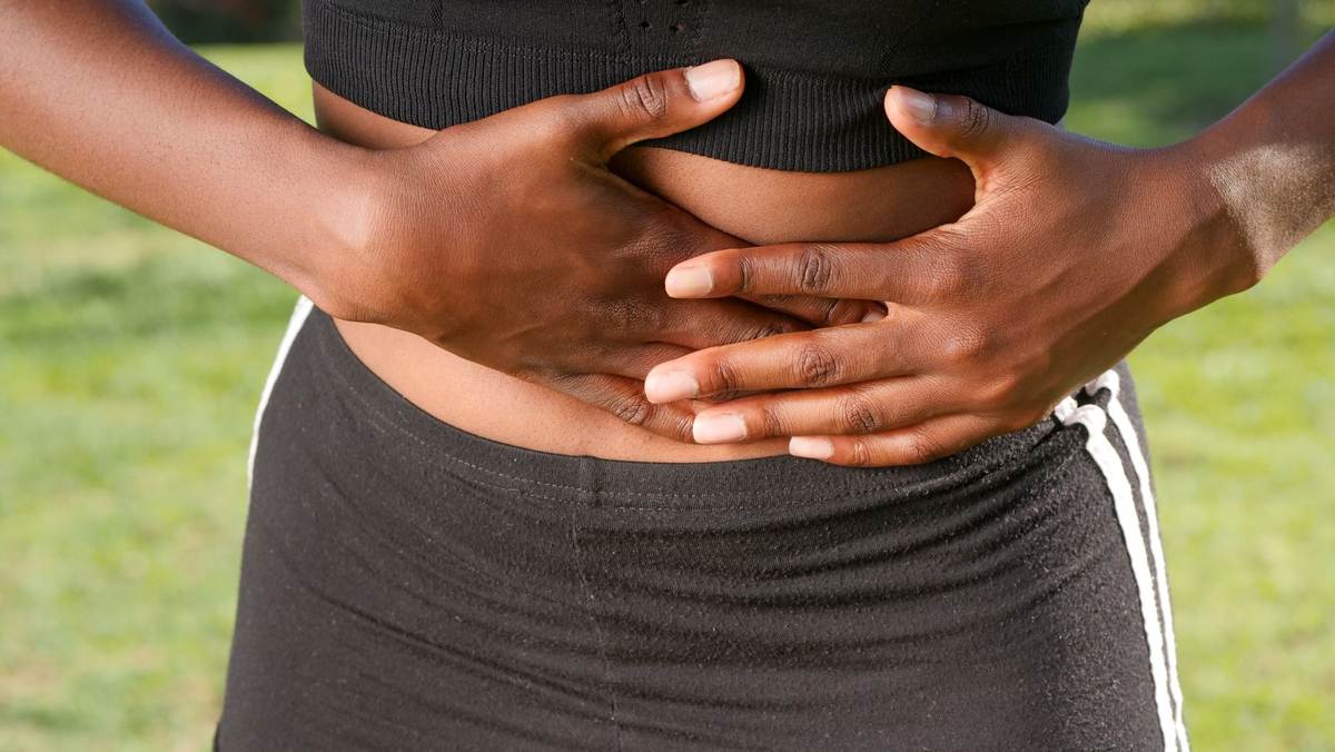 Une personne serre son ventre avec les deux mains sur l'herbe