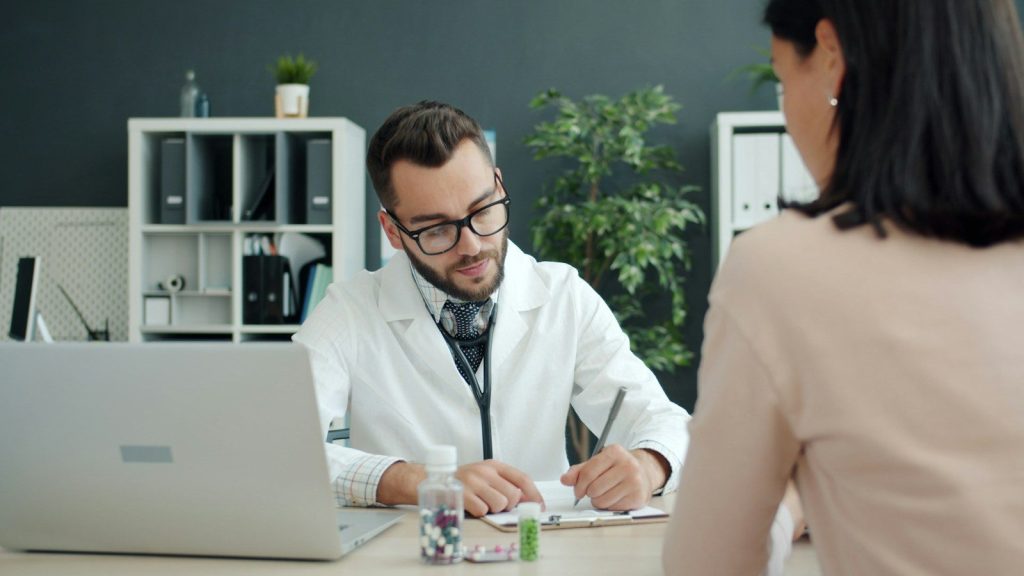Doctor writing notes while patient sits opposite